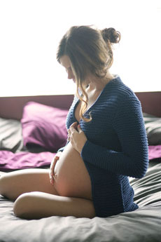 Femme enceinte assise sur sont lit avec main sur le ventre